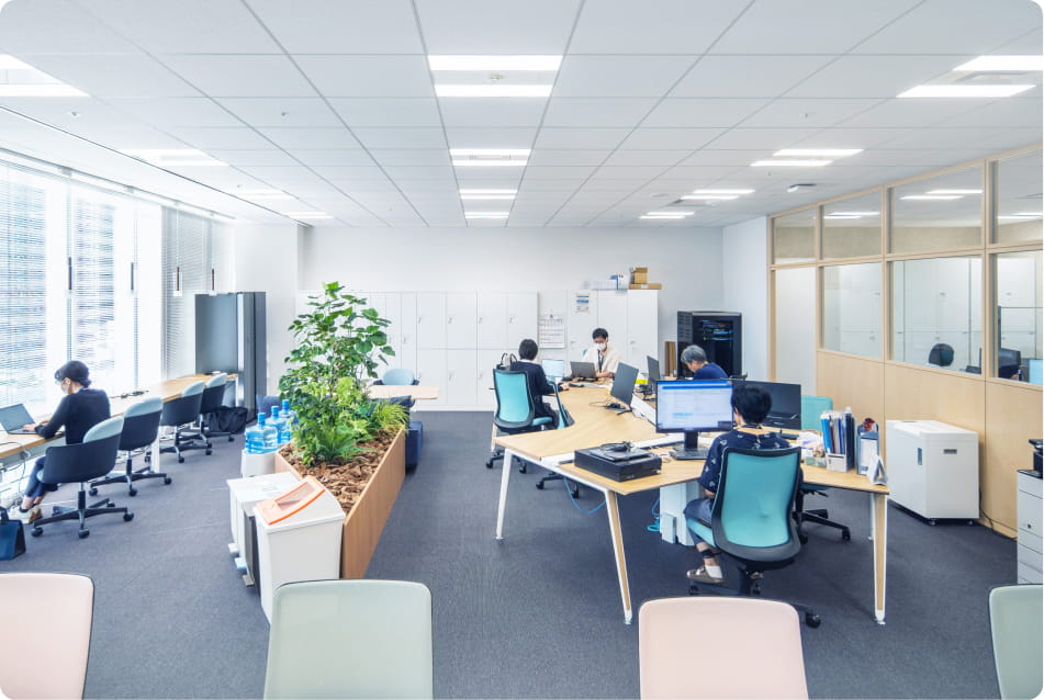 明るく広々としたオフィスで、複数の人がデスクでパソコン作業をしている