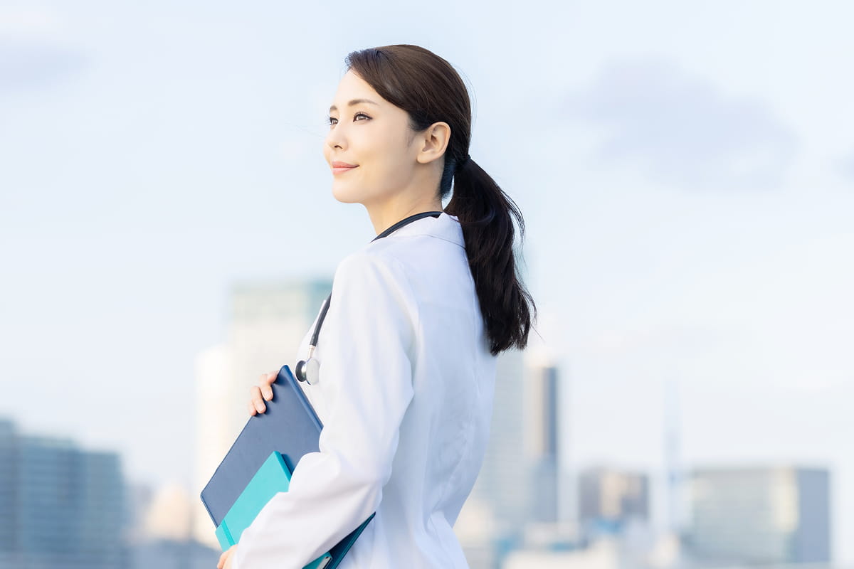 白衣を着た女性が屋外で書類ファイルを抱えて立っている