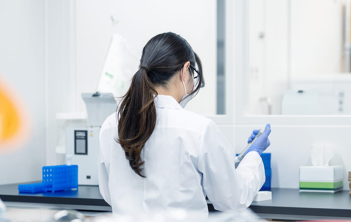 白衣を着た女性研究者が、実験室で器具を扱っている後ろ姿