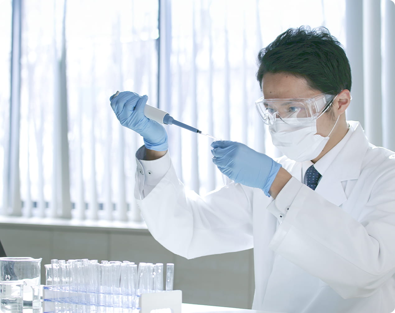 白衣・ゴーグル・マスクを着用した研究者が、ピペットで試薬を扱っている