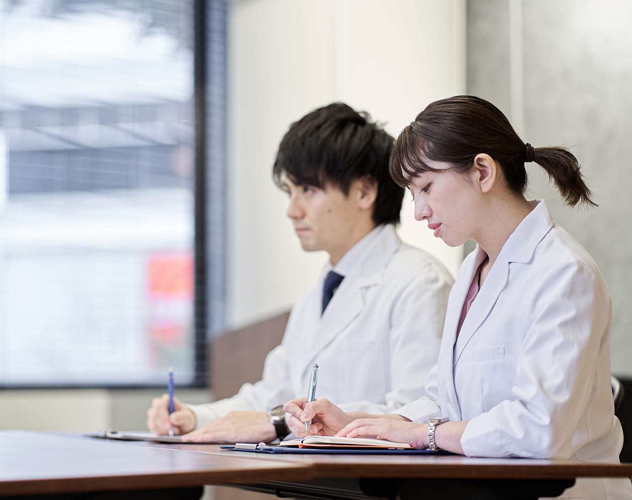 白衣を着た研究職の男女が研修に参加し、ノートを取りながら学んでいる様子