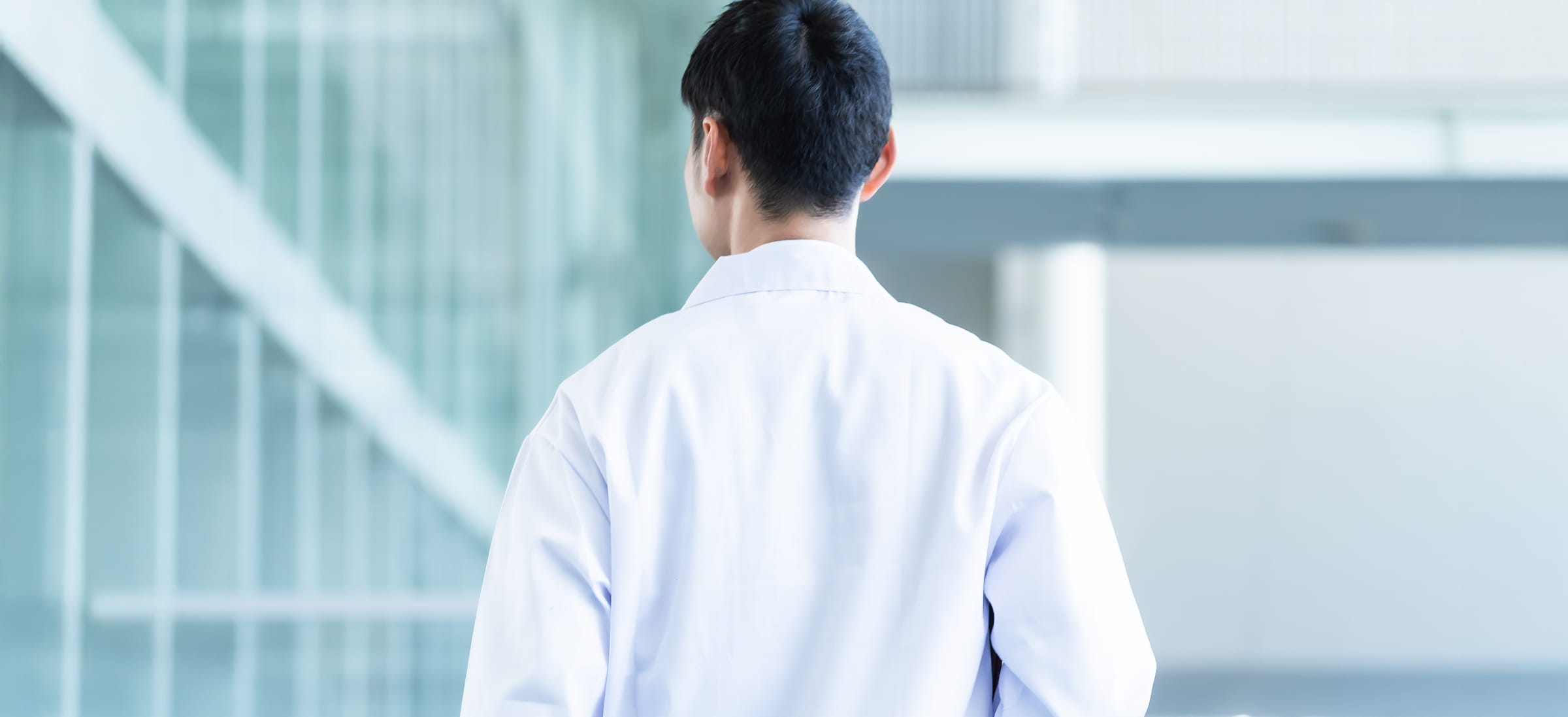 研究施設内を歩く白衣の研究員の後ろ姿。