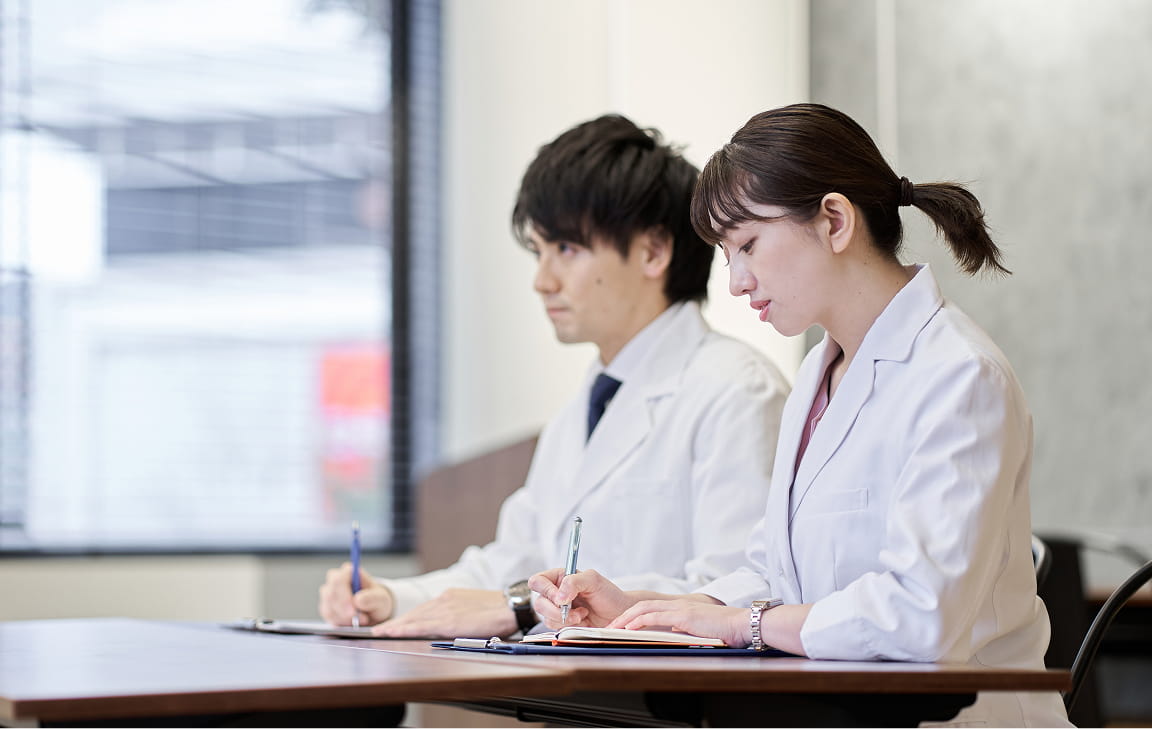 白衣を着た若手研究者が学習や研修に取り組む様子。